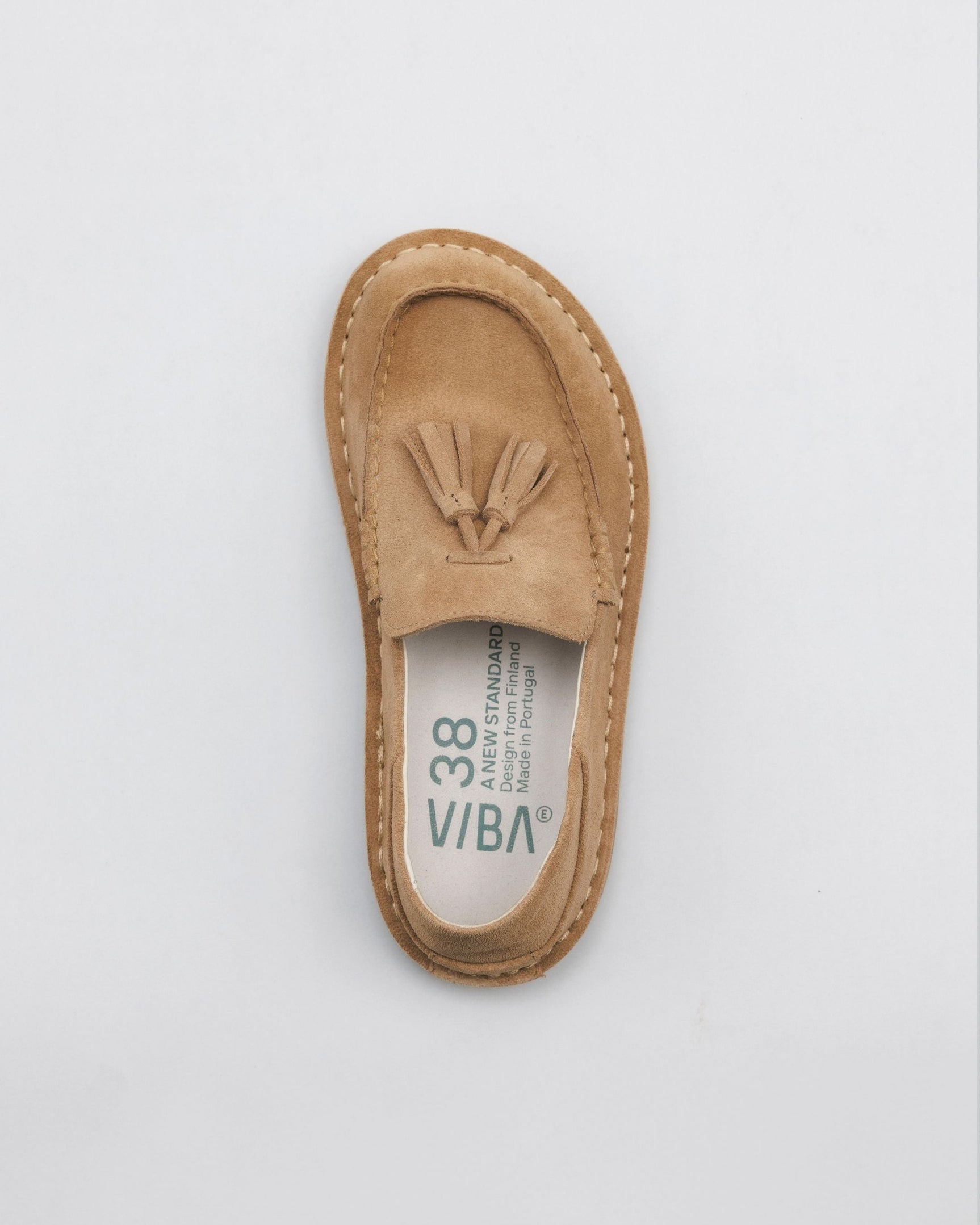 Tan suede loafer with tassel detail and white stitching, shown from top view.